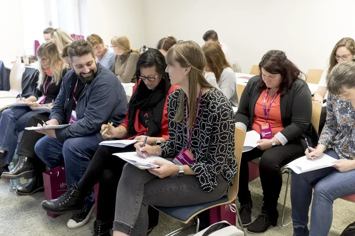 Teilnehemnde in Sitzreihen mit Notizbüchern aus den Goodie-Bags.