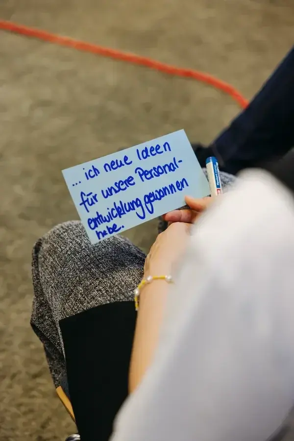 Teilnehmerin hält ein Notizkärtchen in der Hand